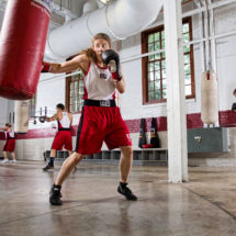 A gym full of boxers training. A female boxer in the foreground practices on a punching bag.
