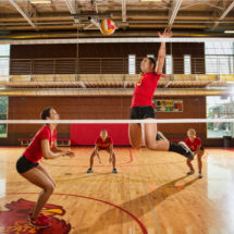 A team of female volleyball players, with the front player about to spike the ball.