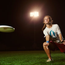 A female ultimate frisbee player throws the frisbee off one knee.